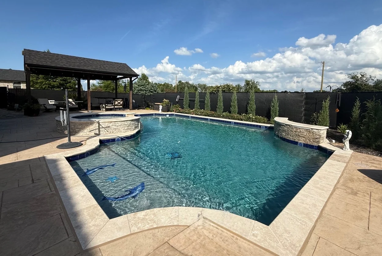 Completed residential pool with tanning ledge, raised stone features, and covered outdoor living by Averra Pools and Outdoor Living